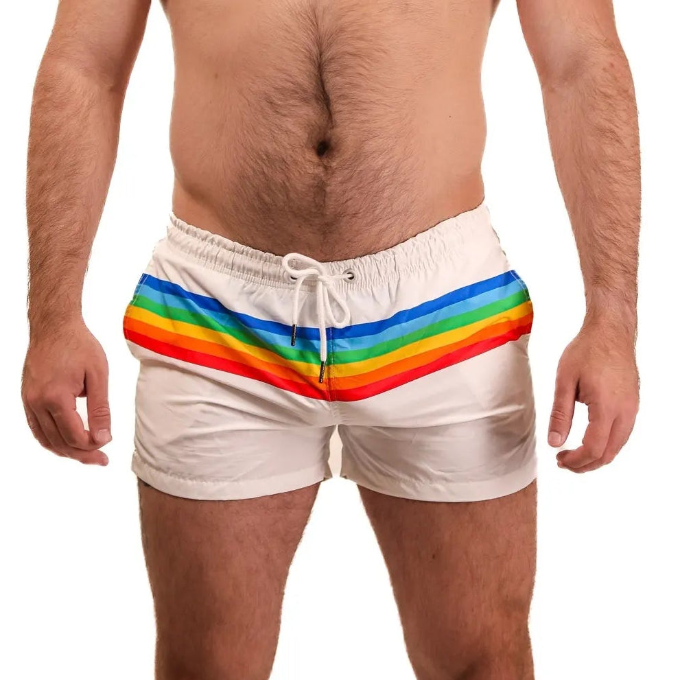 A person standing against a white background, wearing white swim shorts with a rainbow stripe.