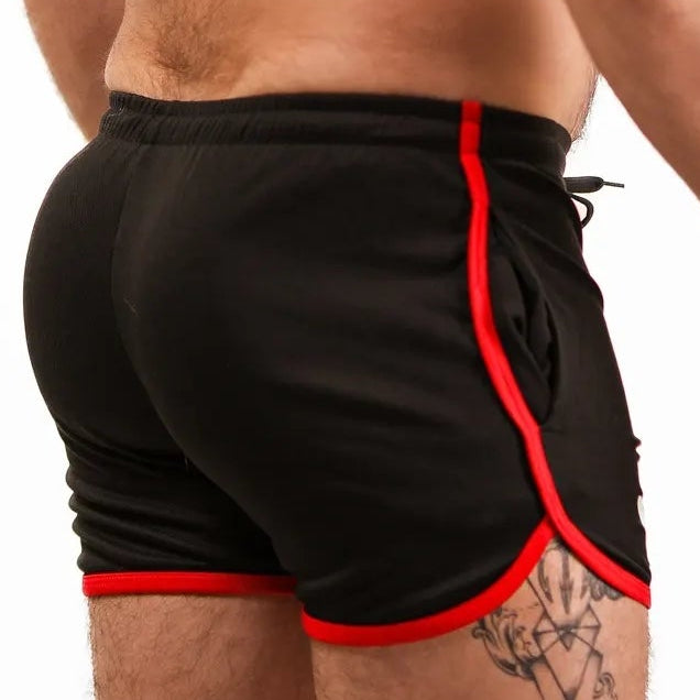 Man wearing black swim shorts with red trim on a white background